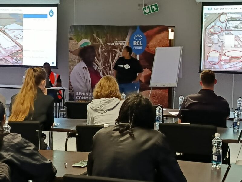 An Ultra-Pet team member giving a speech in-front of attendees sitting in desks, listening in.