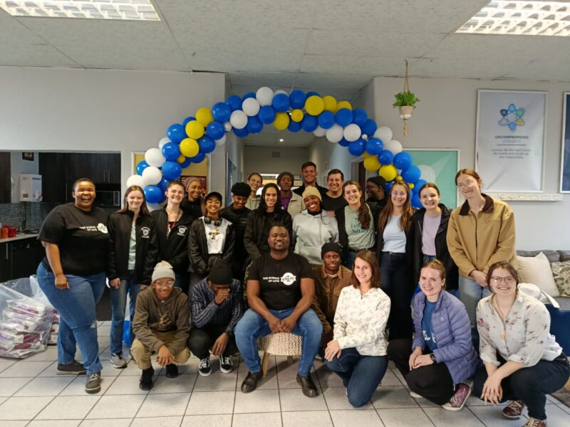 A group photo of the Ultra-Pet team in their office, with their branded colours made into a balloon arch.